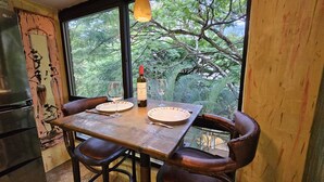 Un comedor con una mesa dispuesta para dos personas, una botella de vino y vistas a árboles a través de amplias ventanas.