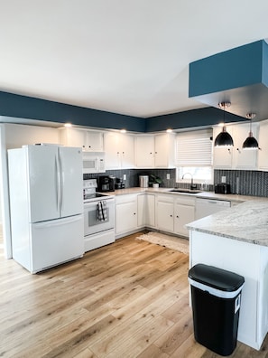 A modern kitchen with white cabinets, a black trash bin, and a wooden floor.