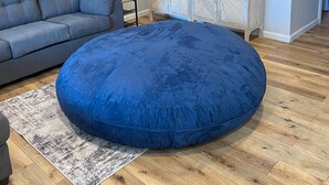 Sala de estar com um sofá cinzento, um puff azul, uma televisão sobre um armário de madeira e piso de madeira.