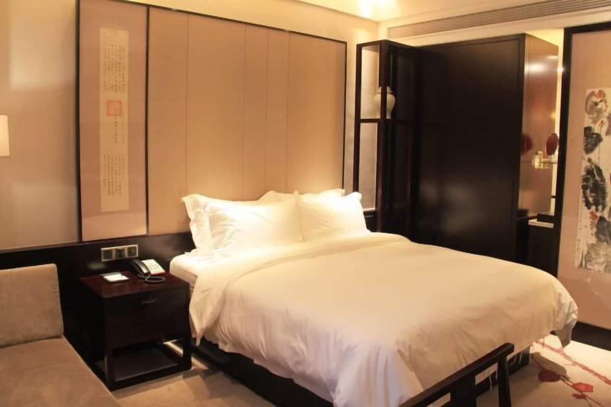 A hotel room with a bed, a bedside table with a phone, a nightstand, and a wall with a framed artwork.