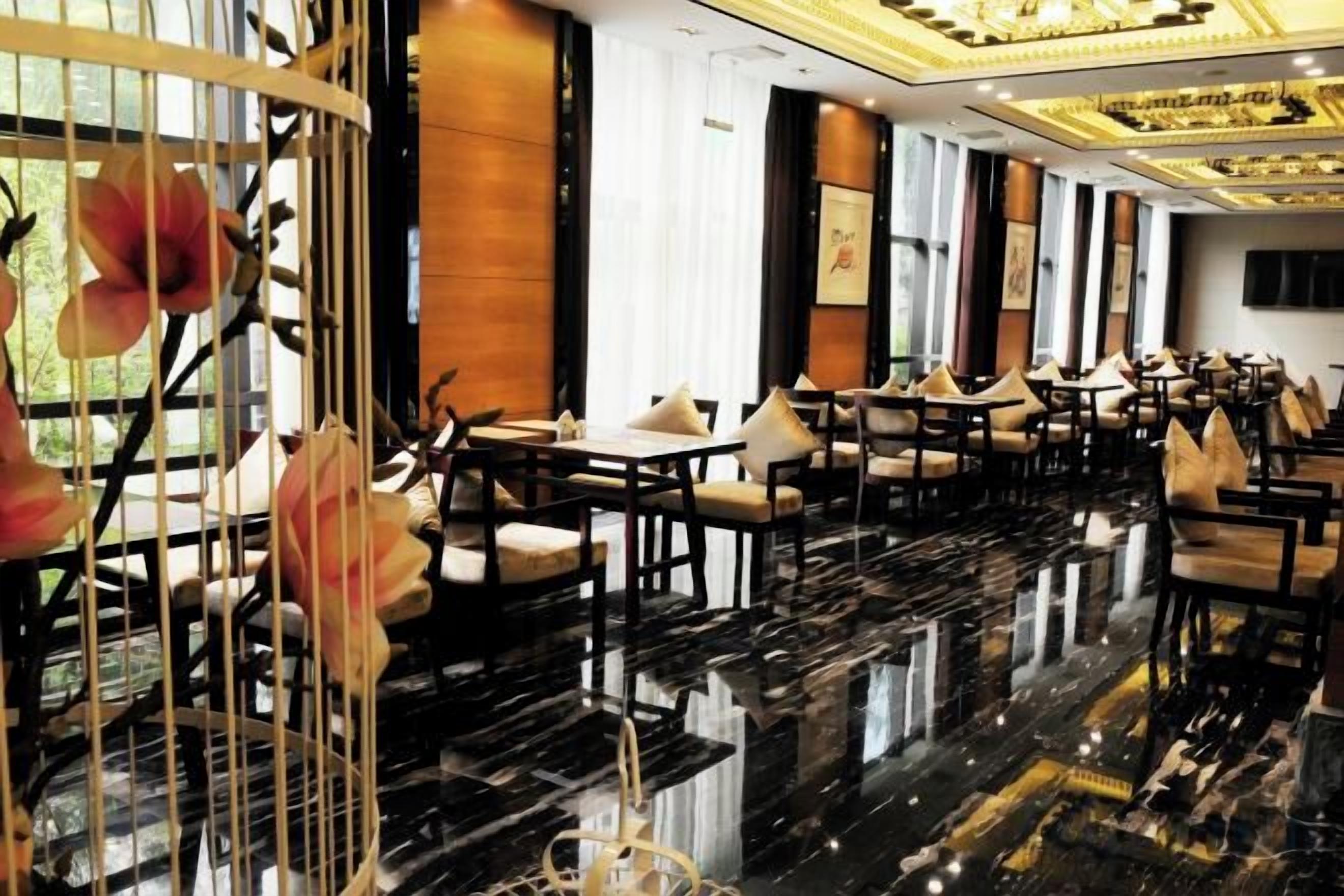 A spacious hotel lobby with a polished black marble floor, numerous tables and chairs, and large windows allowing natural light.