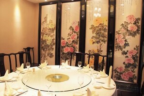 Una mesa redonda dispuesta para una comida, rodeada de sillas, ubicada frente a un biombo con motivos florales.