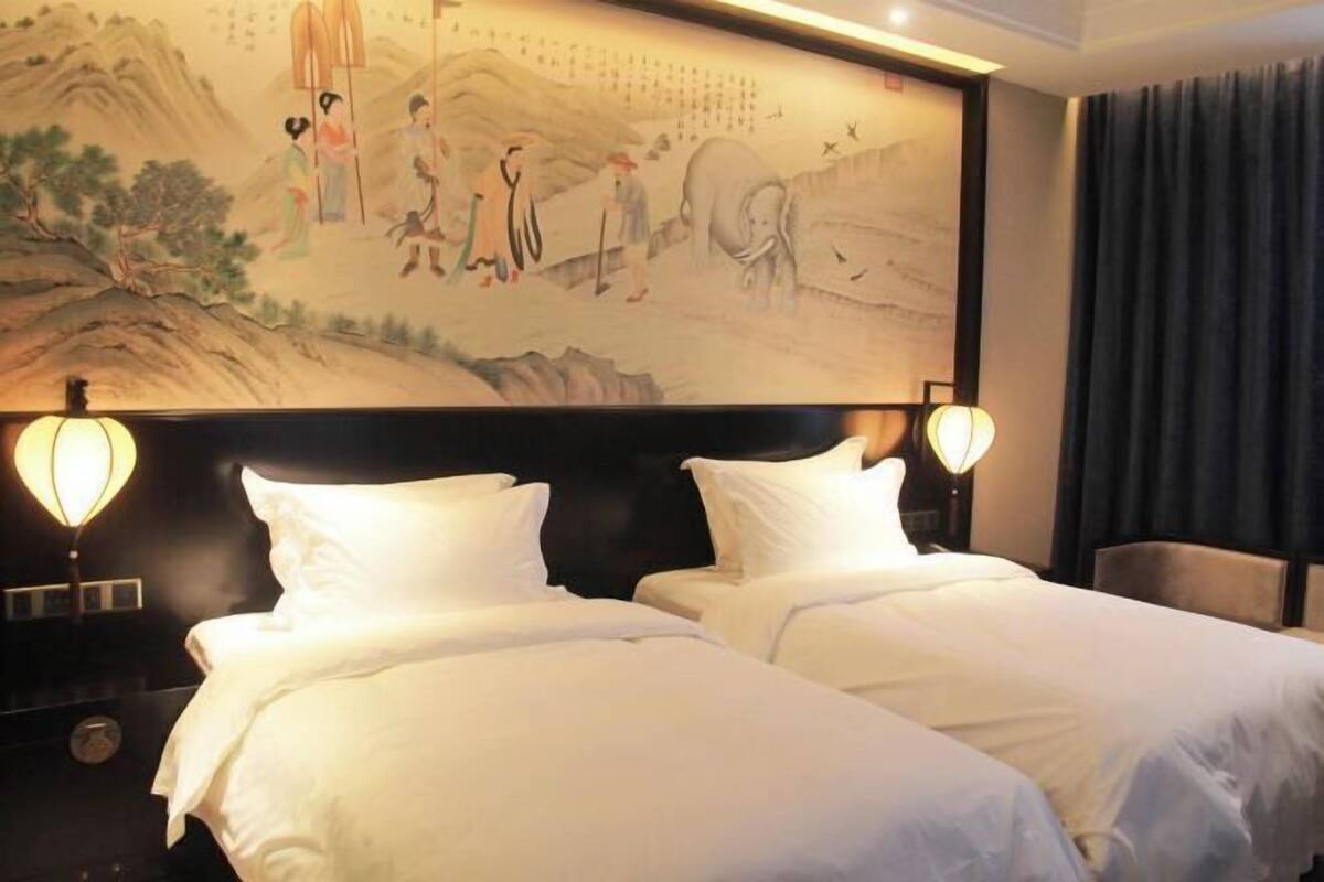 A hotel room with two beds, a large wall mural, and two wall-mounted lamps.