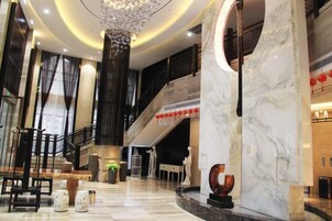 Um saguão de hotel com um balcão de recepção de mármore, uma escadaria e um candelabro.