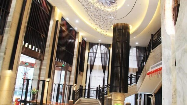 En rummelig lobby med en imponerende trappe, marmorgulv og et dekorativt loft.