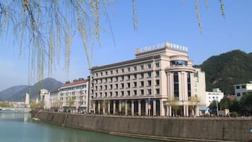 A building with a classical architectural style, located beside a river with a bridge in the background.