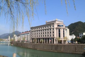Un edificio de estilo arquitectónico clásico, ubicado junto a un río con un puente al fondo.