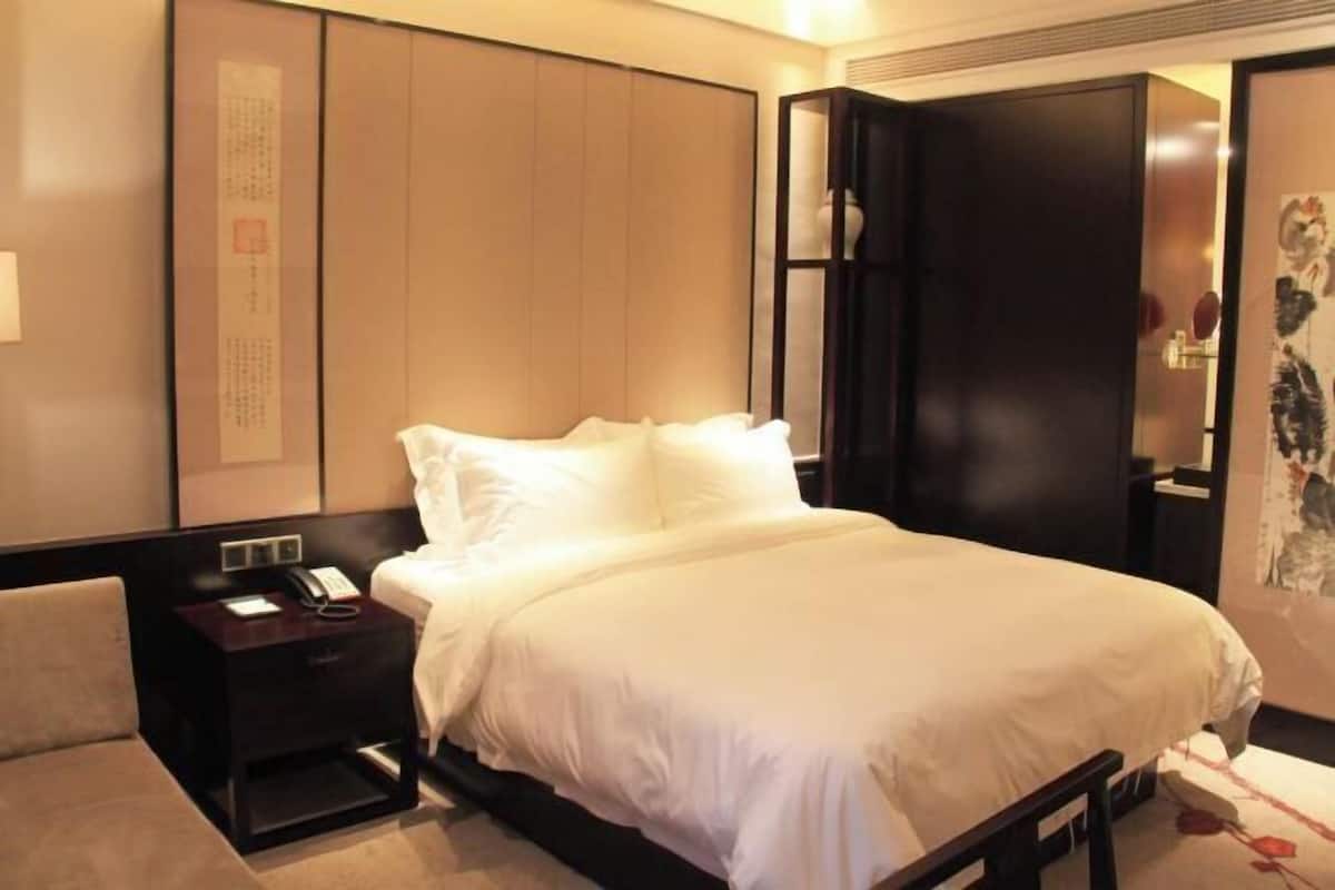 A hotel room with a bed, a bedside table with a phone, a nightstand, and a wall with artwork.