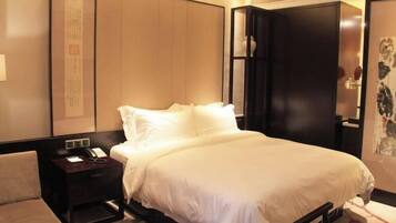 Una habitación de hotel con cama, mesita de noche con teléfono, lámpara y una pared decorada con obras de arte.