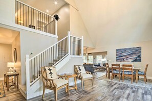 Un espacio habitable amplio con techo alto, una escalera con barandilla y un comedor con sillas y mesa.
