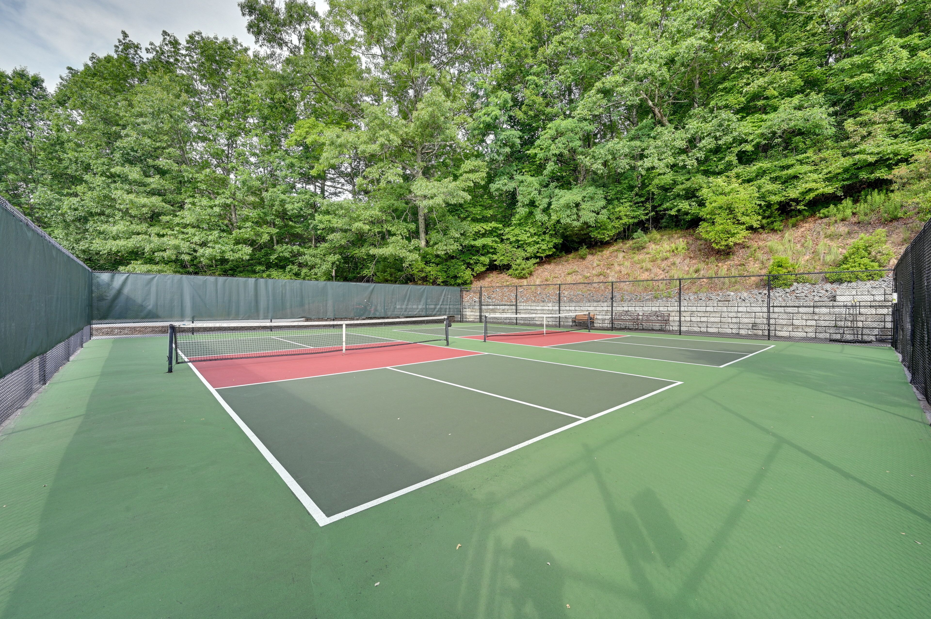 Un court de tennis avec un filet, entouré d’arbres et d  ’un mur de pierre.