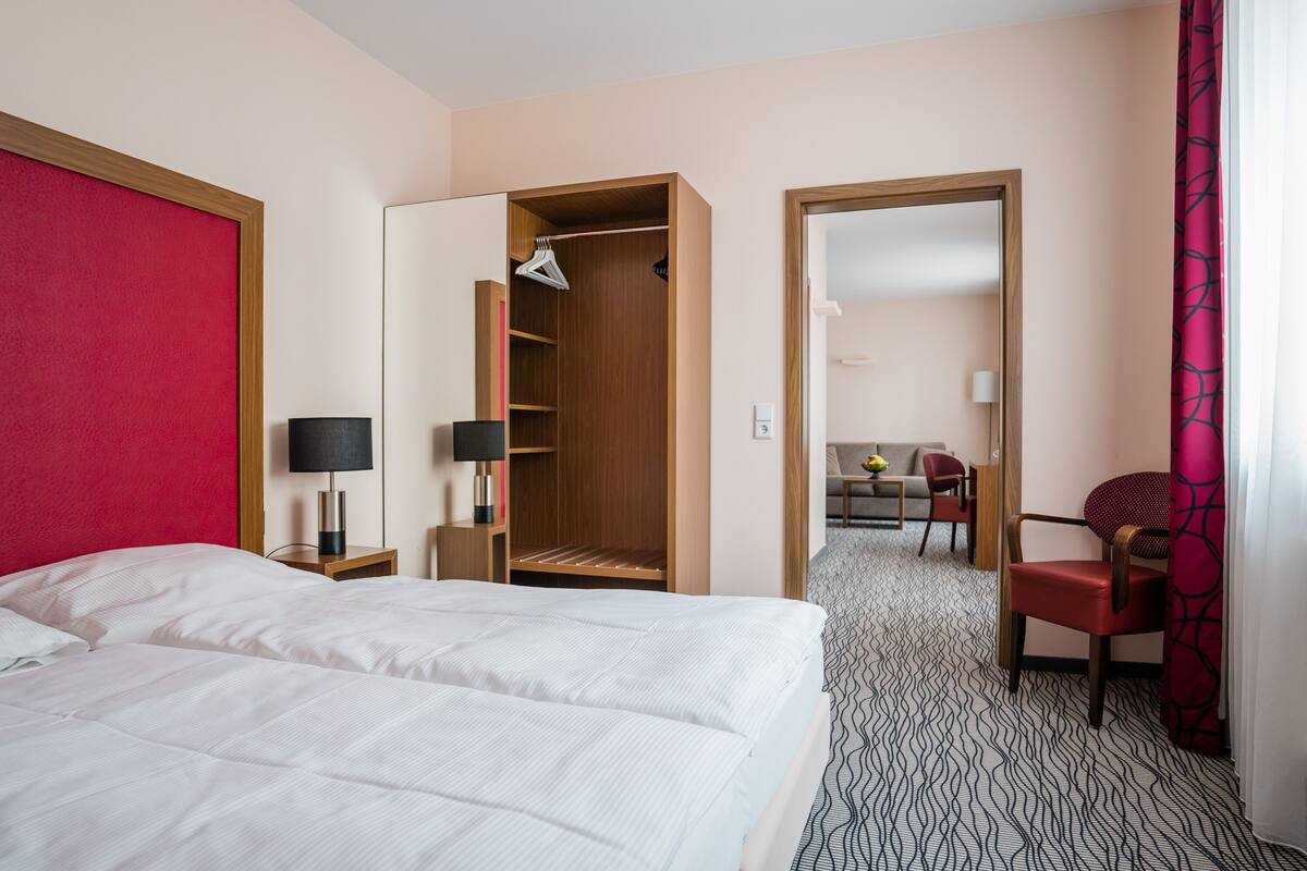 A hotel room with a large bed, a wooden wardrobe, a desk with a lamp, and a chair.
