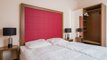 A hotel room with a bed, two bedside tables, a red headboard, a wardrobe, and a mirror.