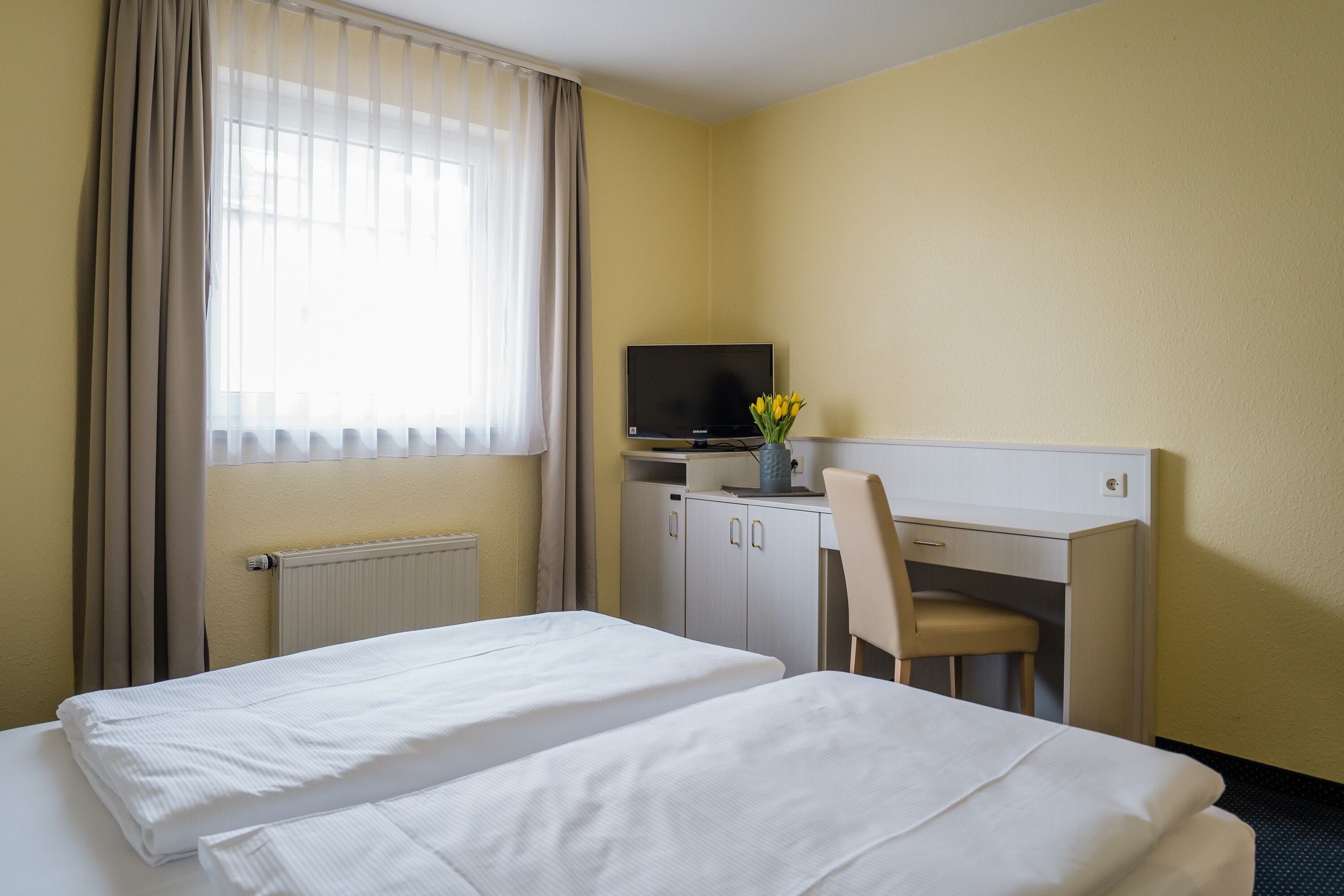 A hotel room with two beds, a desk with a chair, a television, and a window with curtains.