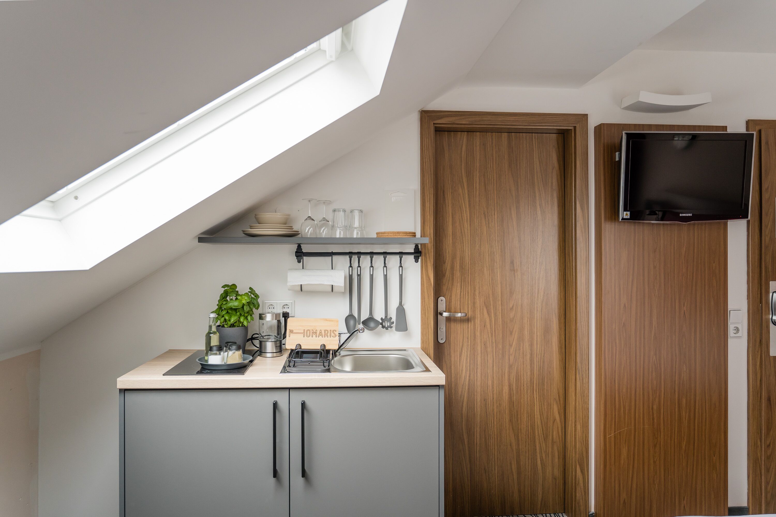 Une cuisine compacte dotée d’un puits de lumière, d’une porte en bois et d’un téléviseur fixé au mur.