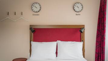 A hotel room with a bed, two clocks labeled 'Dresden' and 'Berlin', and a red curtain.