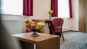 A room with a wooden table, a bowl of fruit, a chair, and a window with red curtains. - Point Hotel Apartments & Rooms (Dresden)