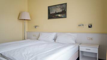 Een hotelkamer met een bed, nachtkastje, lamp en een schilderij aan de muur.