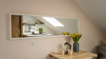 A kitchen with a large mirror, a wooden table with two cups, a coffee maker, and a vase with yellow flowers.
