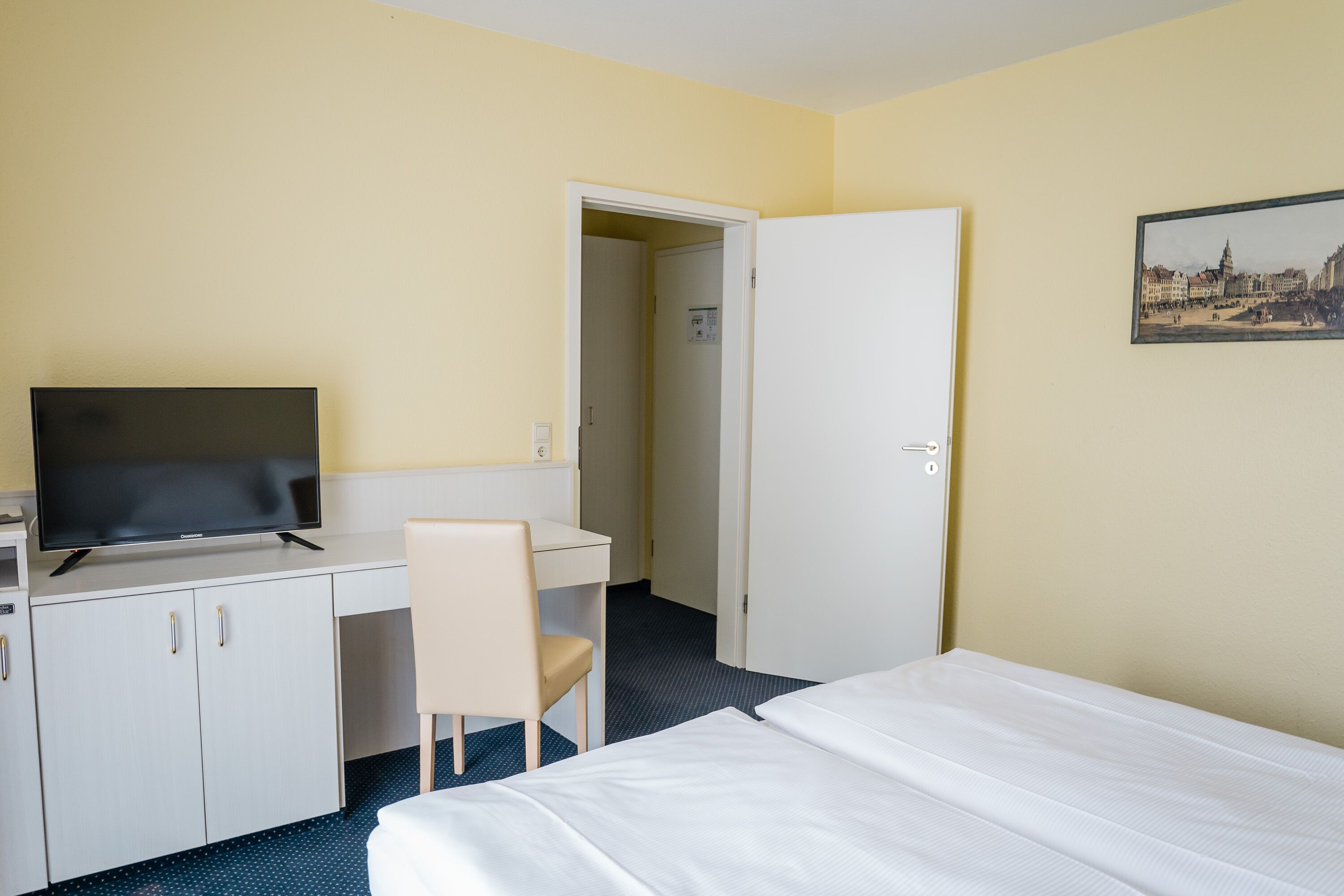 Une chambre d’hôtel comprenant un lit, un bureau avec une chaise, une télévision et une porte donnant sur une autre pièce.