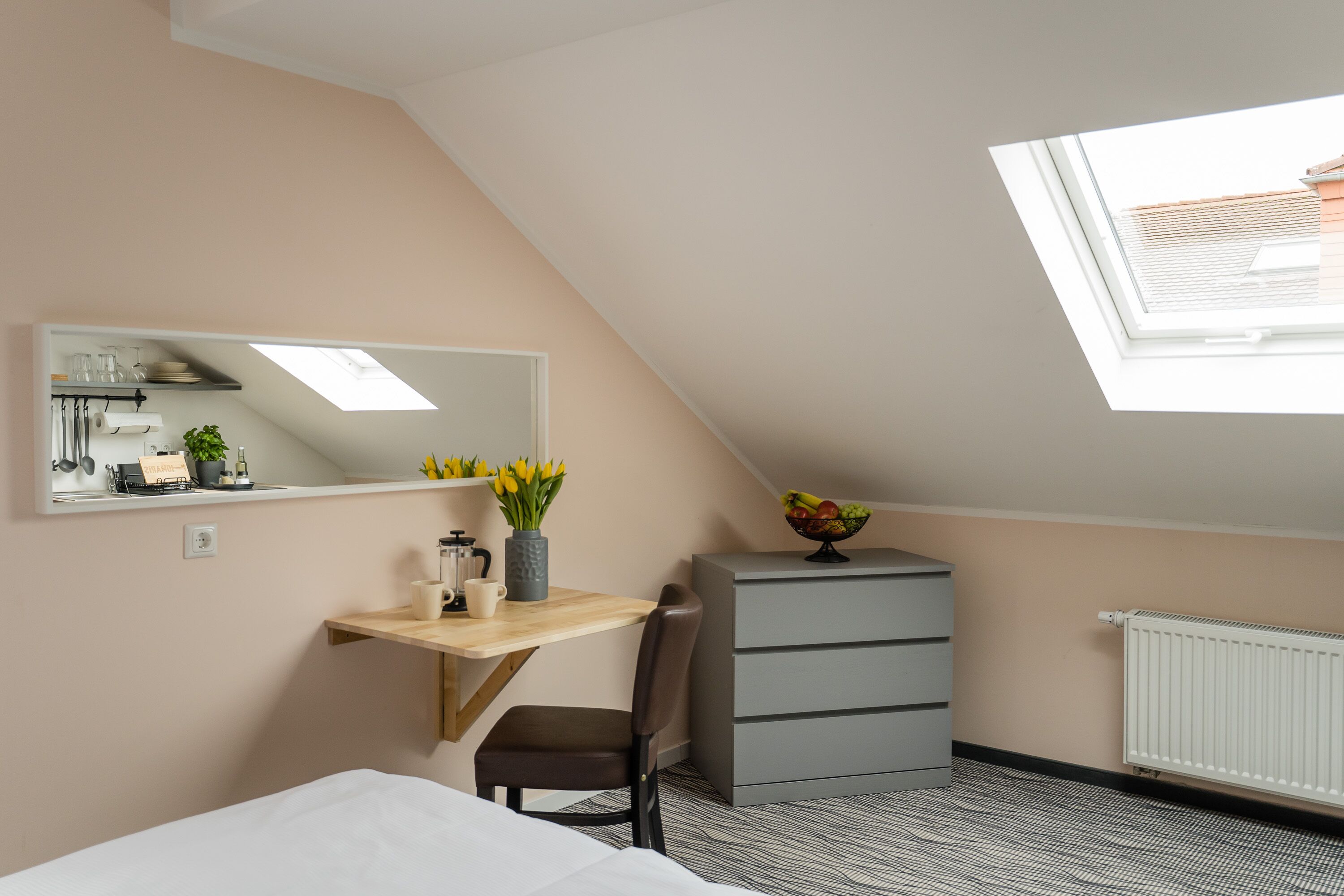 A bedroom with a skylight, a desk with a vase of flowers, a radiator, and a bed.