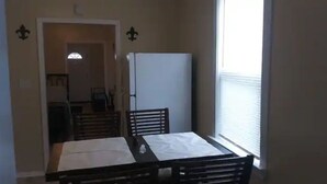 A dining area with a table and chairs, a refrigerator, and a window with blinds. - Lovely Midtown Home Close To ALL Downtown Action (New Orleans)