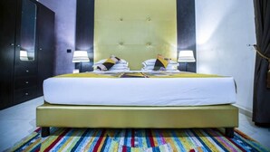 Un lit double avec une tête de lit jaune, deux lampes de chevet et un tapis rayé aux couleurs vives.