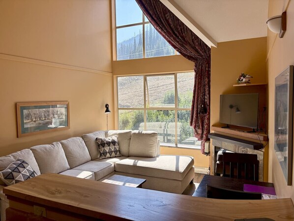 Una sala de estar con un sofá color beige, una mesa de centro de madera, una chimenea y un televisor.