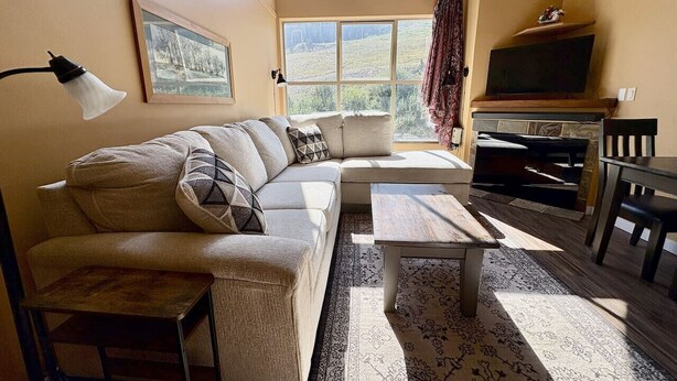 Un salon confortable avec un canapé, une table basse, un téléviseur et une fenêtre avec des rideaux.
