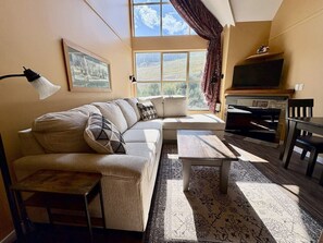 Una sala de estar acogedora con sofá, una mesa de centro, televisor y ventana con cortinas.