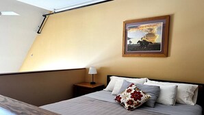 Un lit bien fait, avec une couette grise et blanche, une tête de lit en bois et une table de chevet sur laquelle se trouve une lampe.