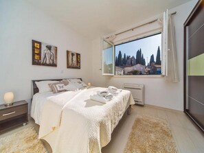 Relax in a serene bedroom with a large bed, framed artworks, and a window offering a view of the surrounding area.