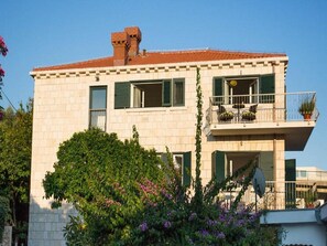 Traditional building with a flat roof and balcony, set amidst lush greenery.