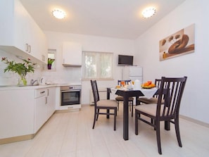 Een moderne keuken met witte kasten, een inbouwoven en een eethoek met een tafel en stoelen.