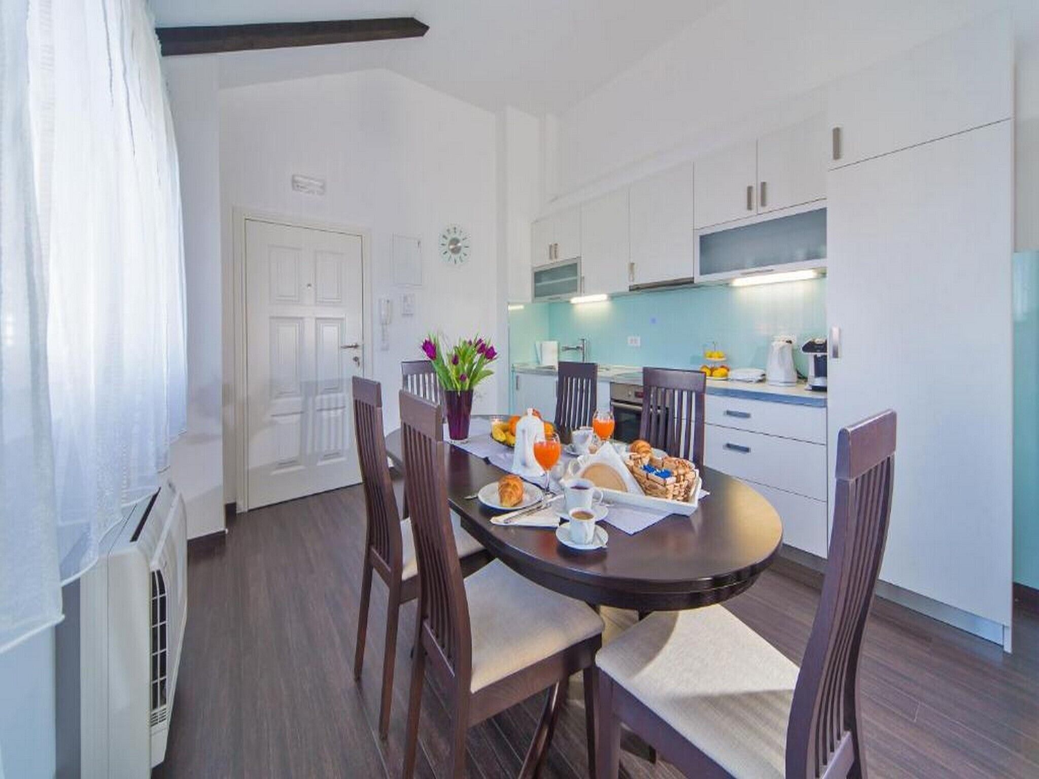 A modern kitchen with white cabinets, a dining table with chairs, and breakfast items on the table.