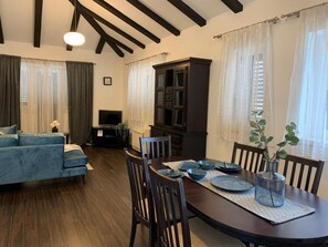 Uma sala de estar acolhedora com um sofá, uma mesa de jantar posta para quatro pessoas e um armário de madeira escura.