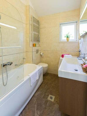 Bathroom features a glass-enclosed shower, bathtub, and toilet, along with a sink and potted plant.