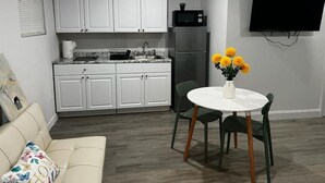 Ein kompakter Wohnbereich mit Küchenzeile, einem Essbereich mit Tisch und Stühlen, einer Couch und einem an der Wand befestigten Flachbildfernseher.