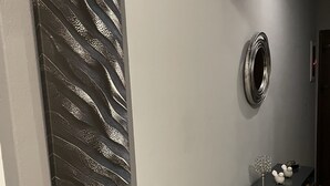 Ein Flur mit einem zeitgenössischen Kunstwerk, einem Zier-Spiegel und einem kleinen Tisch mit Dekoration.
