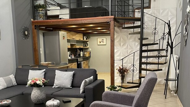 Ein modernes Wohnzimmer mit Sofa, Sessel, Couchtisch und einer Treppe, die in ein Obergeschoss führt.