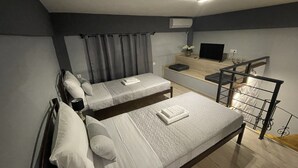 Ein Schlafzimmer mit zwei Einzelbetten, einem Schreibtisch, einem Flachbildfernseher, einem kleinen Tisch und einem Fenster mit Vorhängen.
