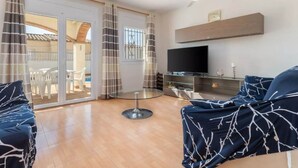 Ein Wohnzimmer mit Fernseher, Sofa und Glastisch.