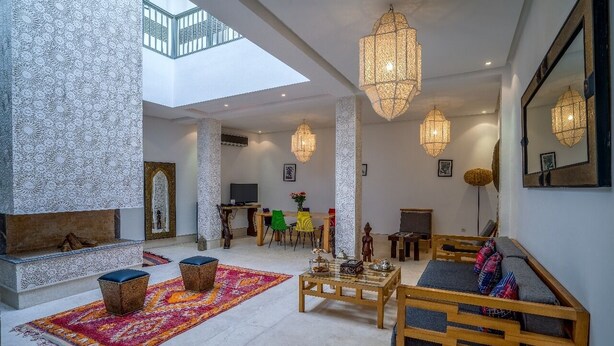 A spacious living area with a high ceiling, a fireplace, and a seating area with a sofa and ottomans. - Riad Bensaleh 56 (Marrakech)