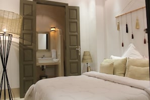 A bedroom with a bed, a bedside lamp, a mirror, and a door leading to a bathroom. - Riad Bensaleh 56 (Marrakech)