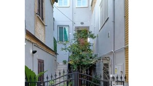 A narrow alleyway with a black wrought iron gate, a small tree, and a building with a window and shutters. - Moments of Serenity (Rocca San Giovanni)