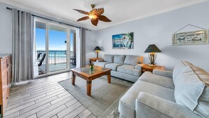A spacious living area with a balcony, a ceiling fan, a sofa, a coffee table, and a painting. - 🏖️Beach Front, Great Views-Twin Palms 402🏖️ (Panama City Beach)