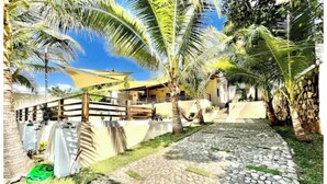 A paved pathway leading to a building with a wooden fence and palm trees. - ATAMI- BEST PRIVATE BEACH HOUSE IN SURF CITY
walk to EL Tunco, El Zonte, Sunzal (La Libertad)