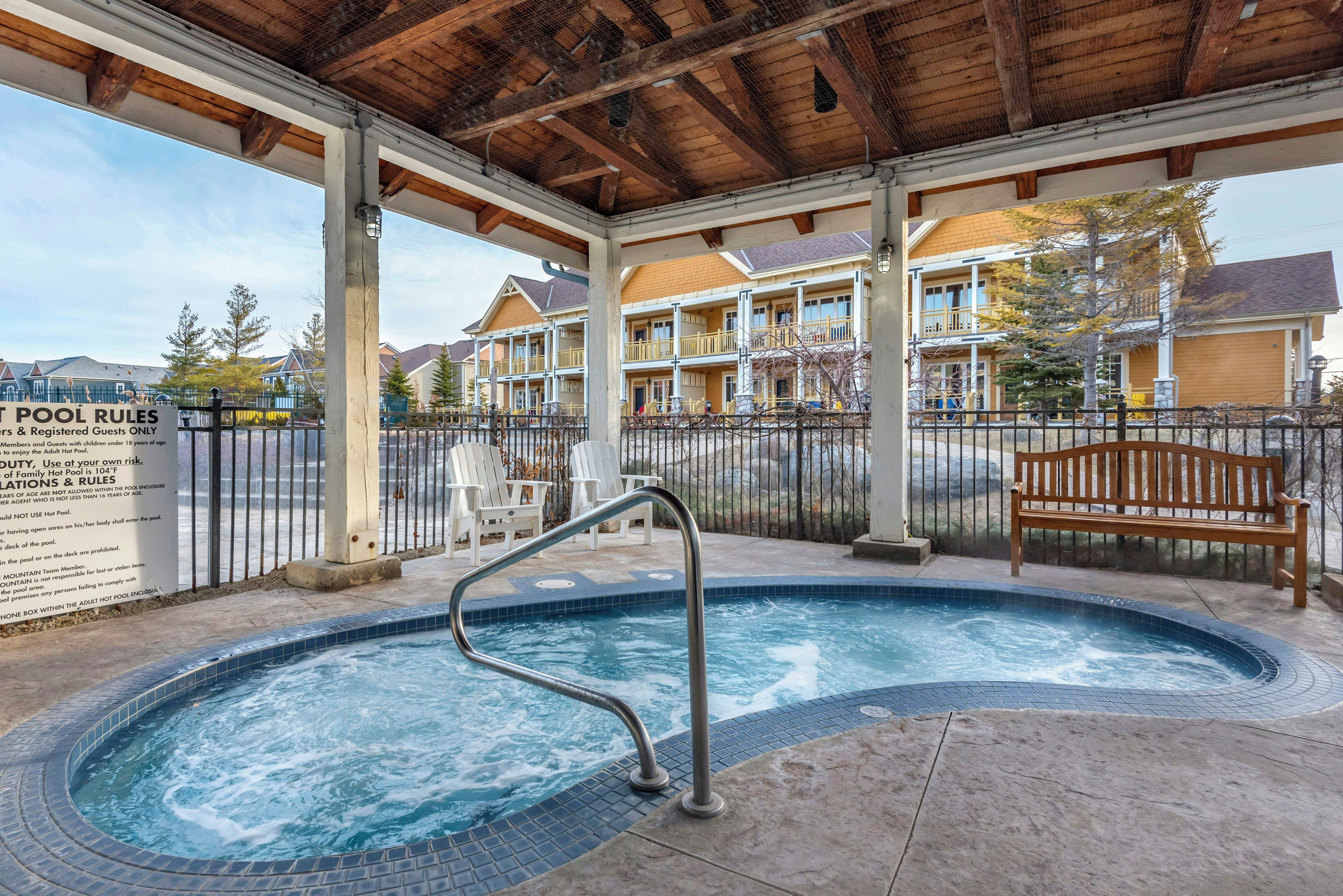 A hot tub with a metal ladder, a wooden bench, and a fenced pool area with a sign detailing pool rules.