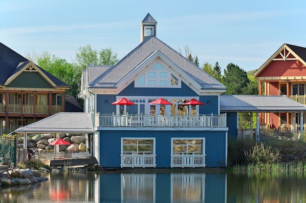 A blue building with a balcony and red umbrellas, situated by a calm body of water. - Hilton Grand Vacations Club Blue Mountain Canada (The Blue Mountains)