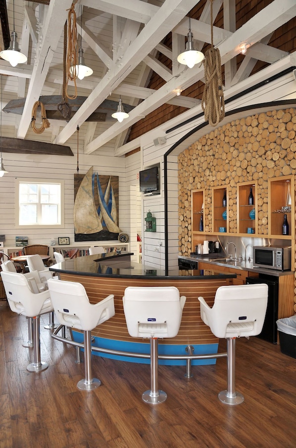 A bar area with white bar stools, a wooden floor, and a stone wall with shelves. - Hilton Grand Vacations Club Blue Mountain Canada (The Blue Mountains)